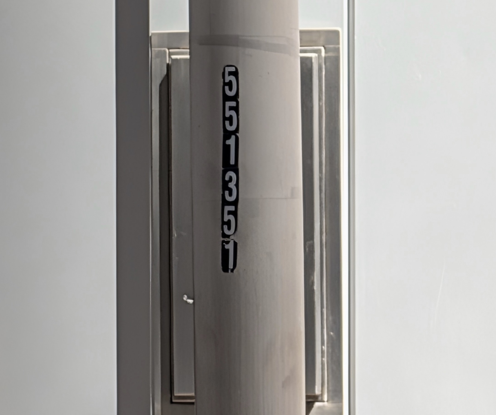 Close-up of a gray utility pole with the serial number 551351 stenciled vertically in white digits on a black label
