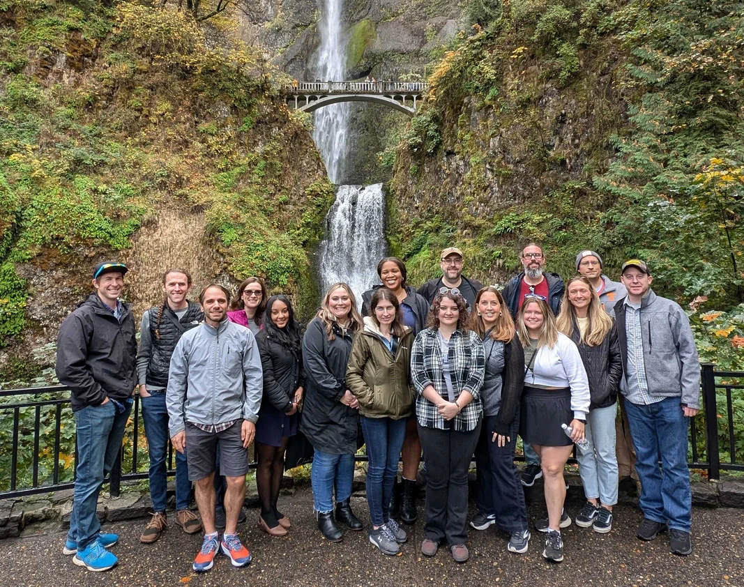 The dymaptic GIS team group photo at Multnomah Falls in the Columbia River Gorge, representing the diverse staff behind dymaptic's ArcGIS solutions